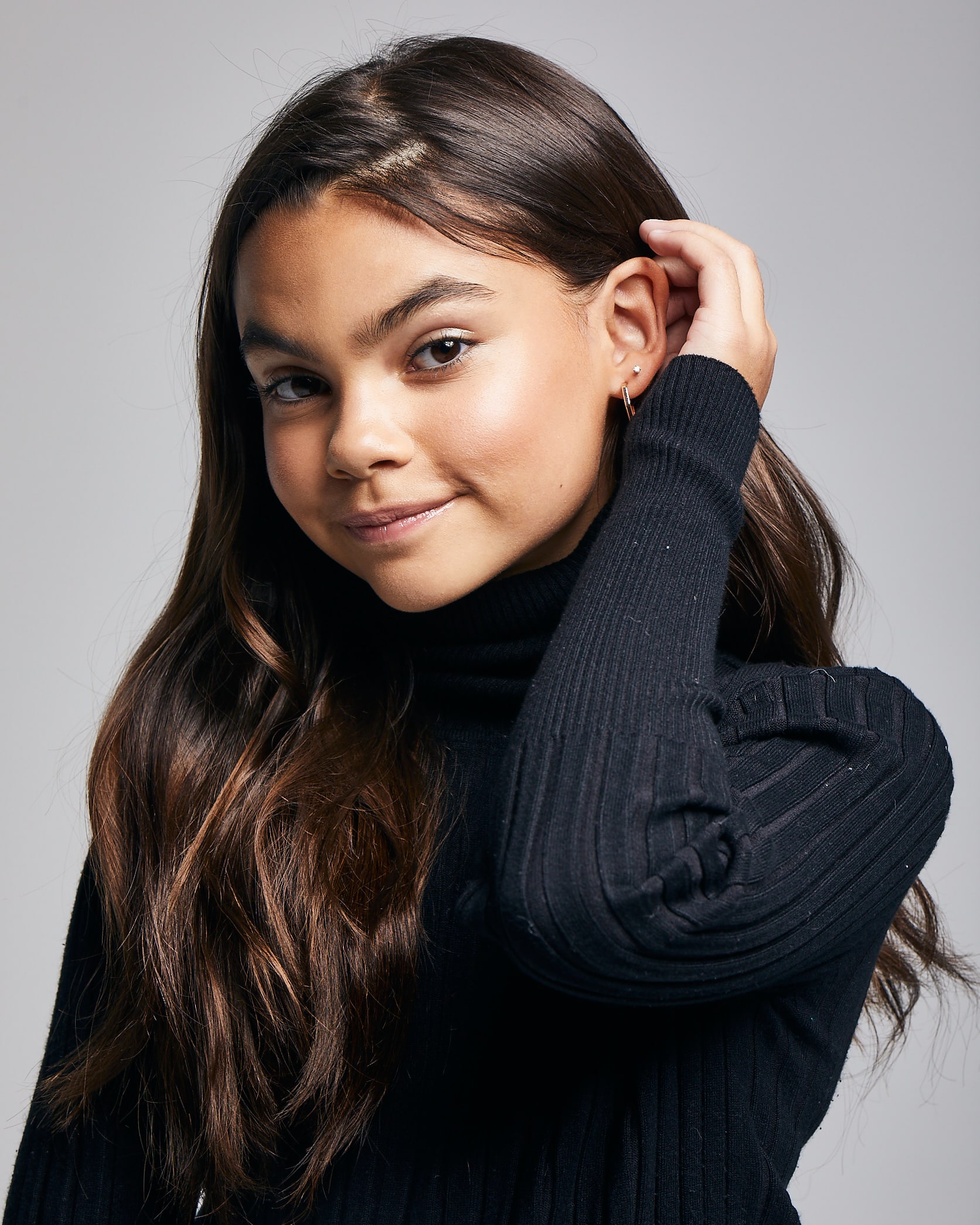 Ariana Greenblatt posing for photograph with her one hand in her hair wearing black sweater 