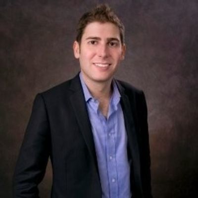 The pic shows Eduardo Saverin is a black suit and a blue shirt.