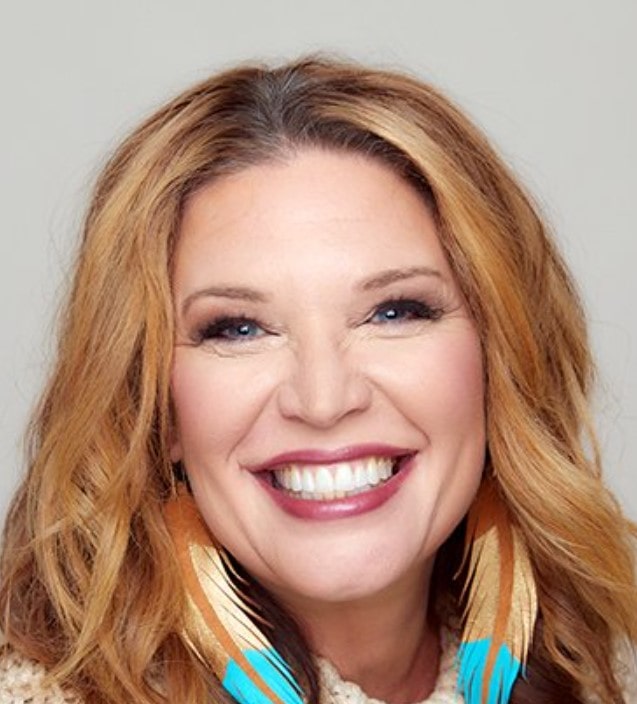 Jen Hatmaker in blue and yellow feather earring smiling in brown hair.