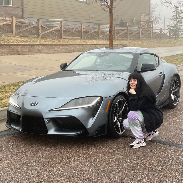 Marrissa Cloutier sitting next to her grey Supra wearing a black sweater and grey trousers