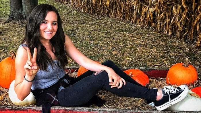 Sydney Golic posing for photo showing her two fingers and sitting in a ground.