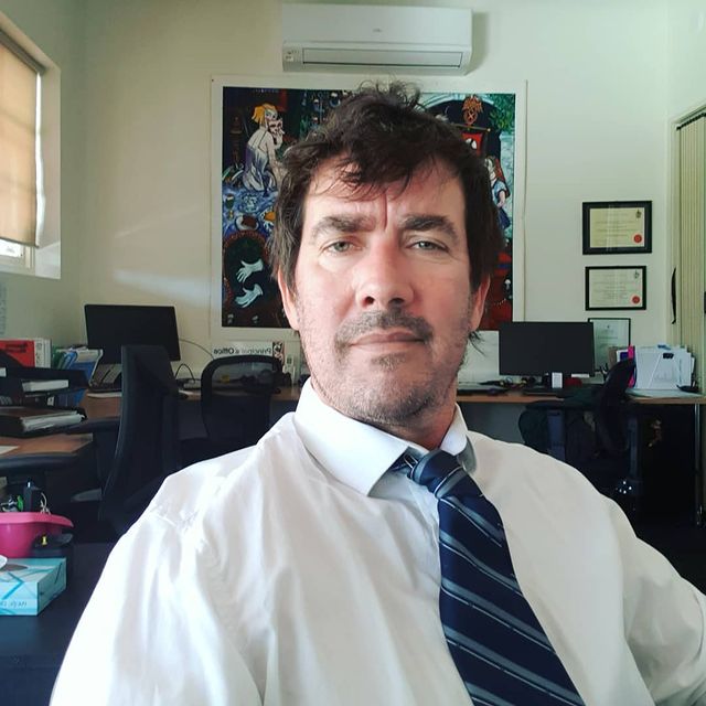 JOnathan Brugh posing for his instagram sitting on chair wearing with white shirt and tie