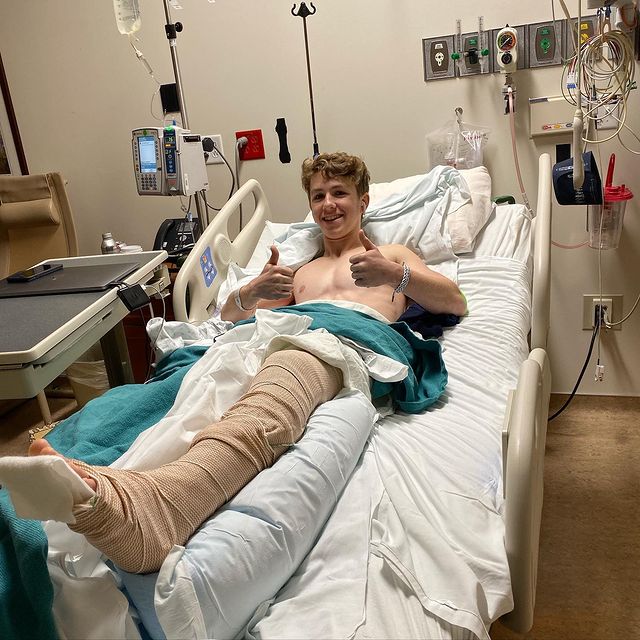 Ethan Wacker posing with the thumb finger up of both hand and laying down in the hospital bed