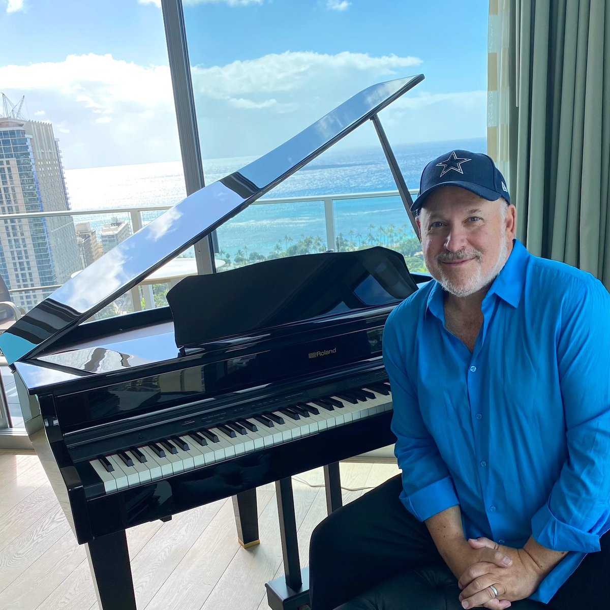 Frank Wildhorn was captured in a smiley face wearing black cap and blue shirt with a harmonium in front of him