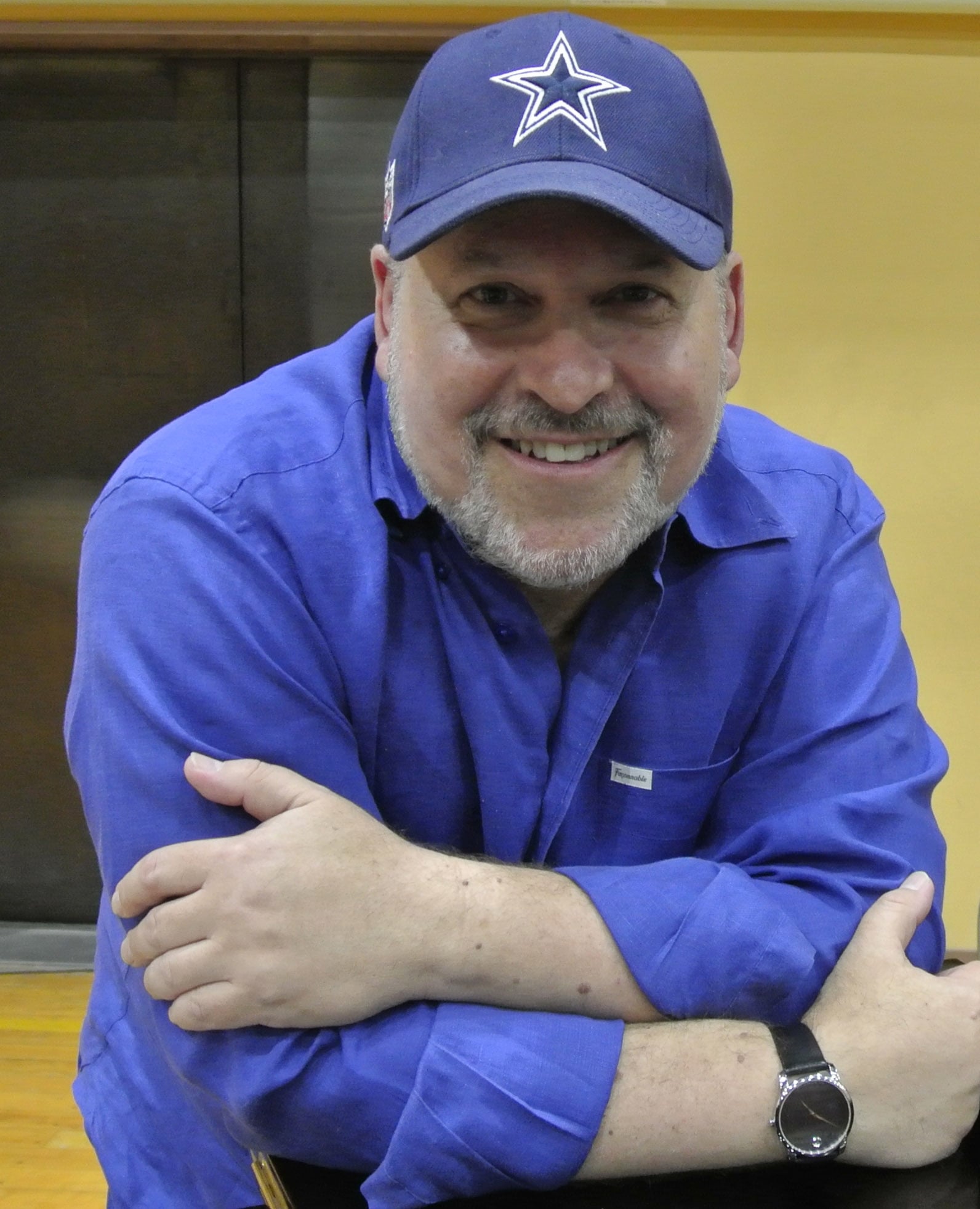 Frank Wildhorn was captured in a smiley face wearing blue cap and blue shirt with a smile face and folding his hand