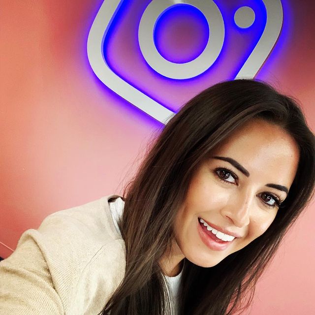 Picture of Kaylee Hartung posing in front of the Instagram logo wearing white color dress