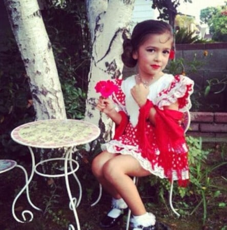 Photo of Maria Canal-Barrera in her childhood  in red dress sitting on a chair in a garden