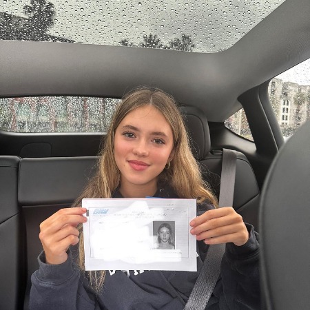 Maisie De Krassel flaunting her driving license while sitting in a car.
