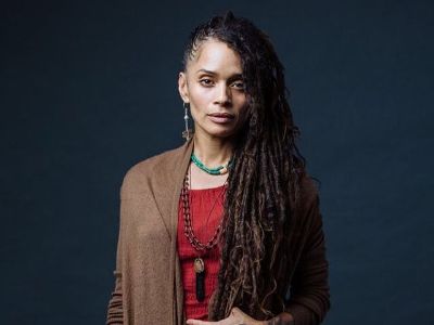 Lisa Bonet is posing in front of a Navy background while wearing a lot of necklaces.