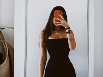 Gabriela Moura is in a black dress taking a selfie while hiding her face.