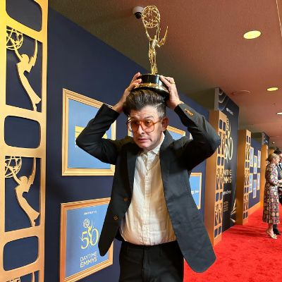 Moshe Kasher holding his Emmy Award over his head.
